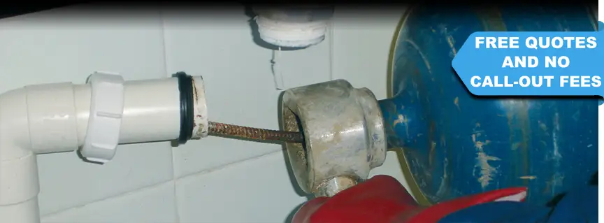 A DRAINTECH engineer cleaning a urinal pipe with a descaling machine that has a coiled cable rotating at high speed